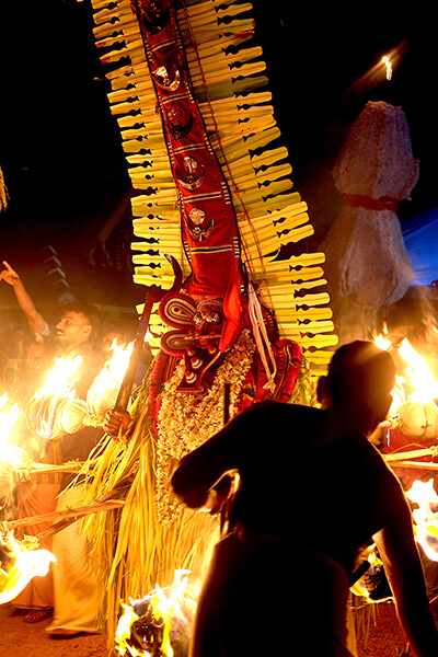 performer in elaborate costume surrounded by fire torches